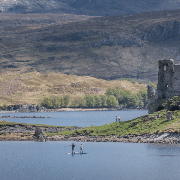 Ardvreck Castle viewed from a distance with people paddling in the loch