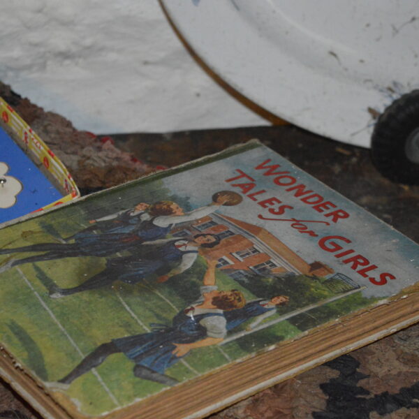 An old, worn book titled 'Wonder Tales for Girls' laid on a table with other toys in the Croft Museum.